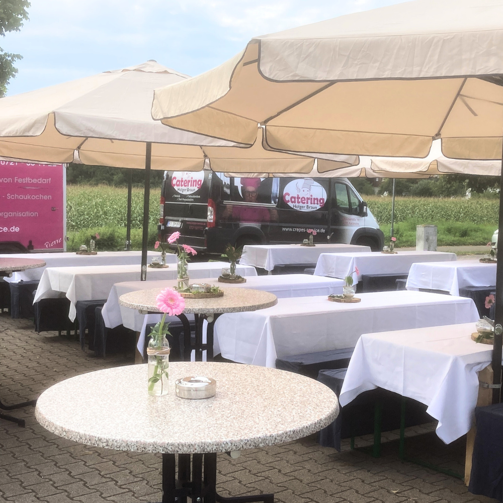 Eventverleih und Partybedarf Festlich gedeckte Tische mit weißen Tischdecken und rosa Gerbera unter großen Sonnenschirmen bei einem Outdoor-Catering-Event von Holger Braun